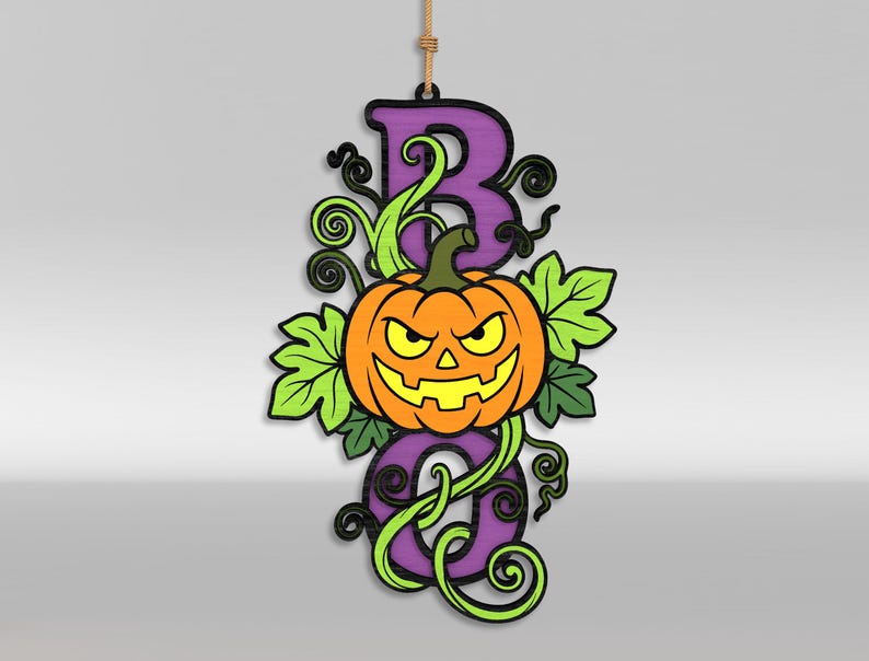 Op de afbeelding: Een hangend houten bord met het woord BOO in paarse blokletters en een oranje jack-o'-lantern pompoen in het midden. Het ontwerp bevat felgroene bladeren en donkere kronkelende ranken, opgehangen aan een dun beige touw.