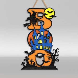 Op de afbeelding: Een verticaal hangbord met de tekst BOO in oranje letters. De B toont een zwarte heks op een bezemsteel en een gele maan met vleermuizen. De O bevat een blauw spookhuis met gele ramen. De laatste O toont zwarte grafstenen en een kale boom.