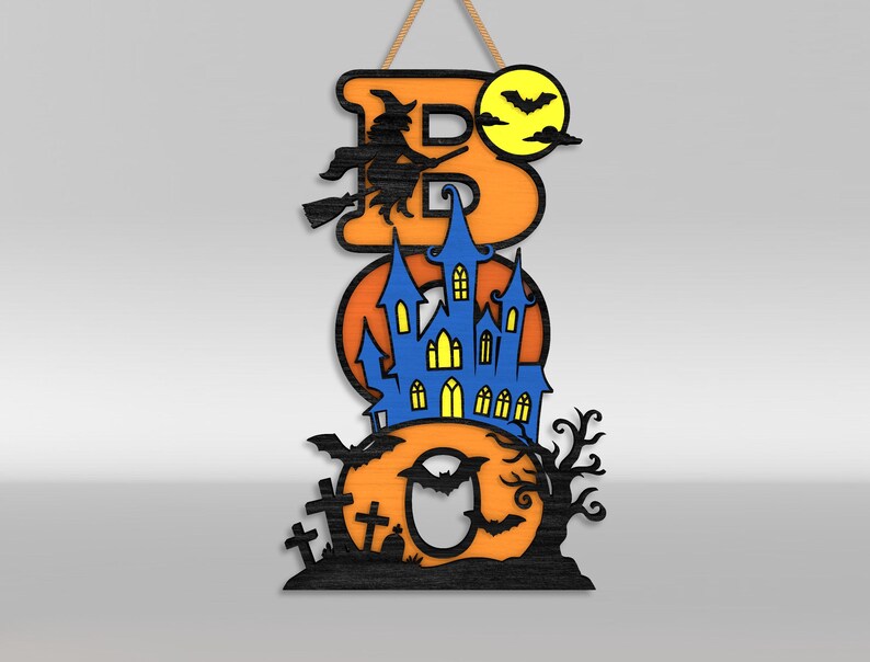 Op de afbeelding: Een verticaal hangbord met de tekst BOO in oranje letters. De B toont een zwarte heks op een bezemsteel en een gele maan met vleermuizen. De O bevat een blauw spookhuis met gele ramen. De laatste O toont zwarte grafstenen en een kale boom.