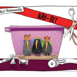 Peut inclure: Une pochette zippée rose avec trois oiseaux de dessin animé portant des couronnes. La pochette est étiquetée "NÄH-SET" et porte un ruban rouge avec le texte "Bio-Baumwolle". L'image comprend également des fournitures de couture comme des ciseaux, du fil et un cutter rotatif.