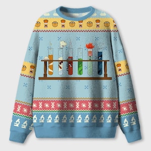 Könnte beinhalten: Ein hellblauer Langarmpullover mit Rundhalsausschnitt und einem sich wiederholenden Muster aus den Gesichtern von Beaker und Dr. Bunsen Honeydew. In der Mitte befindet sich ein braunes Gestell mit sechs Reagenzgläsern mit bunten Flüssigkeiten.