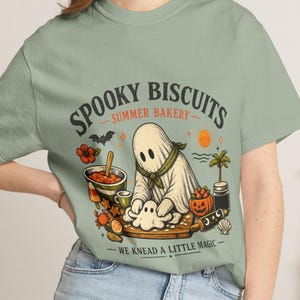Summerween shirt featuring an adorable ghost kneading dough with the playful phrase “Spooky Biscuits.” This Comfort Colors Halloween tee blends spooky bakery charm with sunny summer vibes, perfect for bakers, ghost lovers, Halloween parties, vacations, and seasonal outfits.