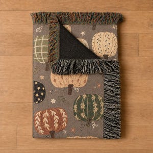 Rustic pumpkin blanket featuring charming patchwork designs, vibrant autumn florals, leafy stems, and earthy seasonal tones. A cozy woven throw with fringe for adding warmth and texture to Halloween decor, fall bedrooms, living rooms, and seasonal displays.