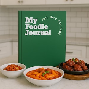May include: A green notebook titled "My Foodie Journal" with white text, alongside bowls of food. The journal reads "just Here for Food". The food includes kimchi, tteokbokki, and fried chicken.
