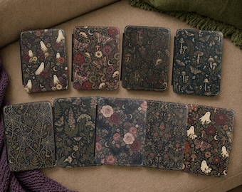 May include: Nine rectangular e-reader cases arranged in two rows, each featuring a distinct dark-toned pattern including ghosts, moths, snakes, flowers, mushrooms, spiderwebs, and bats on a black background with various botanical and celestial motifs.