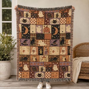 May include: A woven throw blanket featuring a patchwork design with Halloween-themed illustrations including ghosts, black cats, pumpkins, crescent moons, stars, mushrooms, and potion bottles in a color palette of orange, black, purple, and cream.