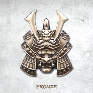 May include: A bronze samurai helmet with intricate details and a fierce expression. The helmet is decorated with a stylised face and horns. The word "BRONZE" is printed below the helmet.