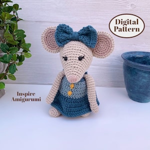 May include: A crocheted mouse doll with a beige body, large pink and beige ears, and a teal bow. The mouse wears a blue and beige dress with yellow buttons. The text "Digital Pattern" is in a brown oval. The text "Inspire Amigurumi" is also visible.