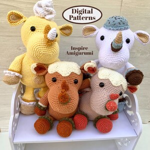 May include: Four crocheted rhinoceros amigurumi toys, each with a different color and design. The toys are sitting on a white shelf with the text "Digital Patterns" and "Inspire Amigurumi" on the shelf.