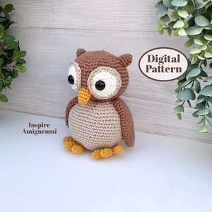 Può includere: Un giocattolo amigurumi all'uncinetto a forma di gufo, realizzato con filato marrone e beige. Il gufo ha grandi occhi neri e un becco giallo. Il giocattolo è seduto su una superficie bianca. Modello digitale.