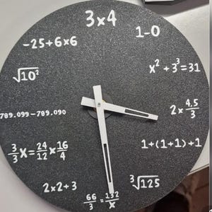 May include: A round, black wall clock with white hands and white numbers and mathematical equations in place of traditional numbers. The clock's hands point to approximately 3:15. The clock has a textured surface.