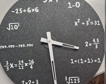 Puede incluir: Un reloj de pared redondo y negro con manecillas blancas y ecuaciones matemáticas blancas en lugar de números. Las manecillas indican aproximadamente las 3:15. La esfera del reloj tiene una superficie texturizada. Diámetro de unos 25 cm.