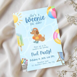 Op de afbeelding: Lichtblauwe zwembadfeestuitnodiging met een teckel met een bril en een zwemband. De uitnodiging bevat de tekst "She's a Weenie Bit older" en "Pool Party!" met datum, tijd en locatie.