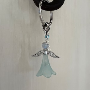 May include: A silver angel charm with a light blue glass flower and crystal accents. The charm is attached to a silver key ring.