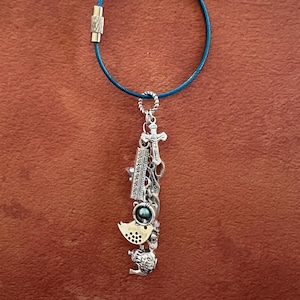 May include: A silver charm necklace with a blue cord. The charms include a cross, a ruler, a bird, and a teapot.