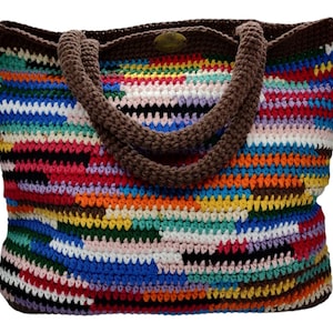 Puede incluir: Un bolso tote de ganchillo hecho a mano y colorido. El bolso presenta un diseño de patchwork vibrante con una variedad de colores, incluyendo rojo, azul, amarillo y verde. Tiene asas y ribetes marrones, y es adecuado para llevar objetos.