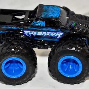 May include: Black and blue monster truck toy with the word "PREDATOR" printed on the side. The truck has large black wheels with blue rims.