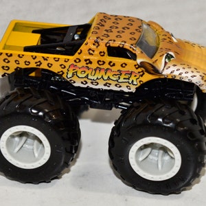 May include: A yellow monster truck toy with a leopard print design. The truck has black wheels with white rims and the words "Pouncer" printed on the side.