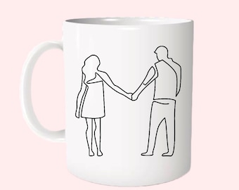 May include: White ceramic mug with a black line drawing of a couple holding hands. The couple is facing each other and is drawn in a simple, minimalist style.