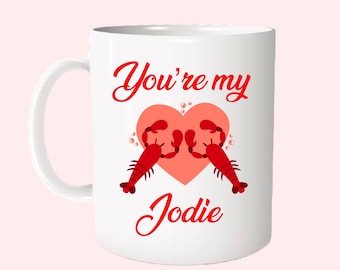 May include: White ceramic mug with a red heart and two red lobsters holding onto the heart. The text "You're my Jodie" is written in red cursive.