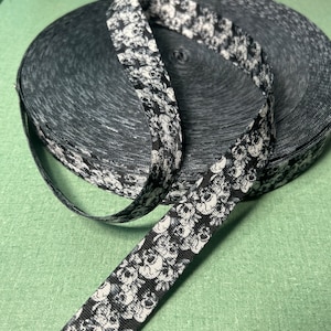 May include: A roll of black and white skull-patterned ribbon. The ribbon is unspooled, revealing the repeating skull design. The roll of ribbon sits on a green surface.