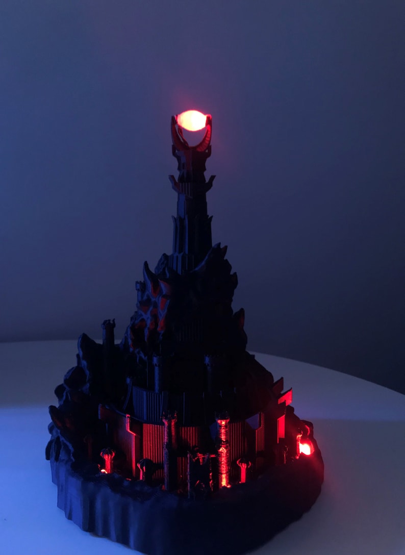 May include: A black 3D printed model of the Dark Tower from the Lord of the Rings, with a red glowing light at the top.