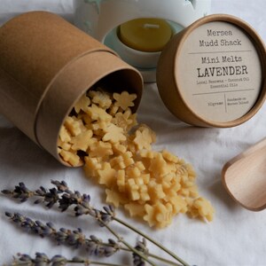 K&ouml;nnte beinhalten: Ein brauner Pappbeh&auml;lter mit Deckel, aus dem sternf&ouml;rmige Wachs-Schmelzen herausfallen. Die Wachs-Schmelzen sind hellgelb. Der Deckel hat ein Etikett mit der Aufschrift "Mersea Mudd Shack Mini Melts LAVENDER Local Beeswax - Coconut Oil Essential Oils Handmade on Mersea Island 50grams".
