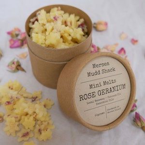 K&ouml;nnte beinhalten: Ein brauner Pappbeh&auml;lter mit einem wei&szlig;en Etikett, auf dem "Mersea Mudd Shack Mini Melts ROSE GERANIUM Local Beeswax - Coconut Oil Essential Oils Handmade on Mersea Island 50grams" steht. Der Beh&auml;lter ist mit kleinen, gelben Wachs-Schmelzen gef&uuml;llt, die wie Sterne geformt sind. Der Beh&auml;lter ist von getrockneten Rosenbl&auml;ttern umgeben.