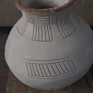May include: A white ceramic vase with a brown rim and geometric patterns carved into the surface.