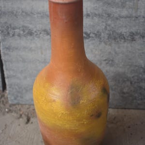 May include: A terracotta vase with a yellow, orange, and green painted design. The vase is tall and narrow with a rounded bottom.