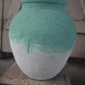 Op de afbeelding: Een grote, ronde, keramische pot met een witte basis en een lichtblauwe bovenkant. De pot heeft een ruw, getextureerd oppervlak en lijkt handgeschilderd te zijn.