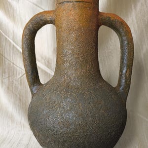 以下が含まれることがあります： 丸みを帯びたボディと円筒形の首を持つ、2つのハンドルが付いた、テクスチャ加工されたアンフォラスタイルの花瓶。 花瓶はざらざらとした土のような質感で、主に濃い茶色で、オレンジと緑のアクセントがあります。 ハンドルは優雅に湾曲しています。