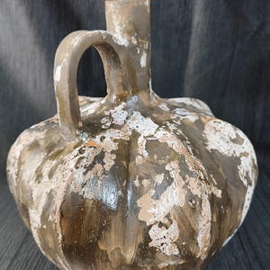 Peut inclure: Une cruche en céramique marron avec une anse et un bec. La cruche a un corps bulbeux avec des rainures verticales et est peinte avec des accents blancs et beiges. La cruche mesure environ 25 cm de haut.