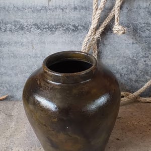 May include: A dark brown ceramic jar with a wide mouth and a rounded body. The jar has a rustic, aged appearance.