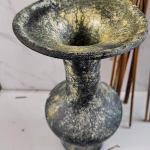 May include: A decorative vase with a wide, flared rim and a bulbous base. The vase has a dark, speckled finish with yellow accents. The vase is a unique piece of home decor.