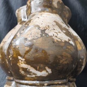 Puede incluir: Un jarrón de cerámica artesanal, bulboso y con una superficie texturizada única. El jarrón presenta una mezcla de tonos marrón, beige y blanco, con un aspecto envejecido y desgastado. El diseño incluye una base redondeada y una parte superior ensanchada.