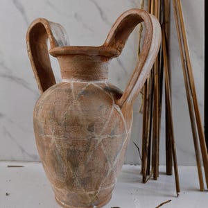May include: A terracotta vase with two handles and a geometric pattern. The vase is a light brown color with white accents.