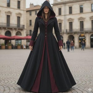 Może przedstawiać: Długi czarny płaszcz z kapturem i bordowymi akcentami. Płaszcz posiada zapinany na guziki przód, długie rękawy z bordowymi mankietami i rozkloszowaną spódnicę. Kaptur i przedni panel są podszyte bordowym materiałem. Płaszcz jest noszony na zewnątrz.