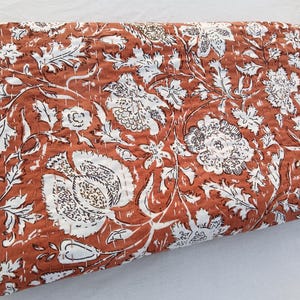 Op de afbeelding: Een roestkleurige kantha-deken met een wit bloemenpatroon. De deken is gemaakt van katoen en heeft een handgestikt ontwerp.