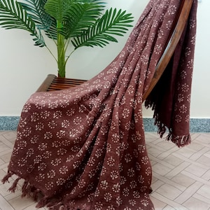 May include: A brown throw blanket with a white floral pattern and fringe trim draped over a wooden chair.