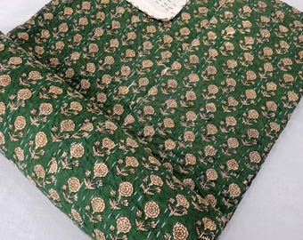 May include: A green floral quilt with a cream-colored border. The quilt features a repeating pattern of beige flowers and is stitched with white thread. The folded corner reveals the cream-colored backing, showcasing the detailed stitching.