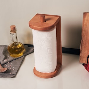 May include: Wooden paper towel holder with a roll of white paper towels. The holder has a natural wood finish and a simple design.