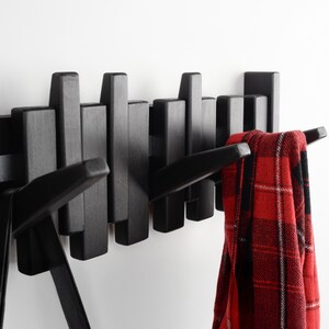 Peut inclure: Porte-manteau mural en bois noir avec plusieurs crochets. Une &eacute;charpe &agrave; carreaux rouge et noir est accroch&eacute;e &agrave; l'un des crochets.