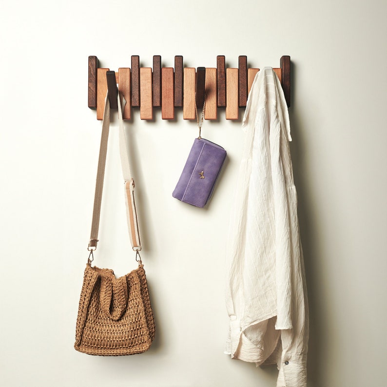 Peut inclure: Un porte-manteau mural en bois avec plusieurs crochets, de couleur bois clair et fonc&eacute;. Un portefeuille violet et un sac en osier brun sont accroch&eacute;s aux crochets.