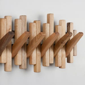 May include: A wooden wall-mounted coat rack with a series of vertical and angled wooden pegs. The pegs are made of light and dark brown wood, creating a natural, textured appearance. The rack is designed for hanging coats, hats, or other items.