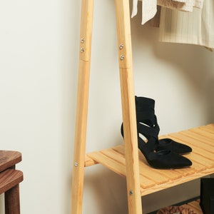 May include: A wooden clothing rack with two shelves and a pair of black heeled shoes on the bottom shelf.
