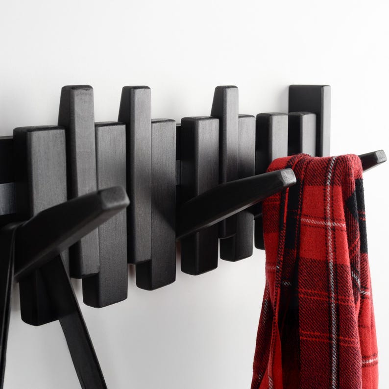 May include: Black wooden wall-mounted coat rack with multiple hooks. A red and black checked scarf is hanging on one of the hooks.