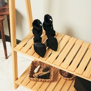 May include: Two pairs of black heeled shoes with criss-cross straps on a wooden shelf with a wicker basket containing hair brushes and nail polish.