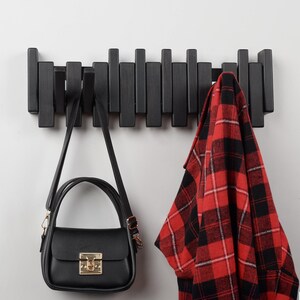 Peut inclure: Un porte-manteau mural en bois noir avec une chemise &agrave; carreaux rouge et noir et un sac &agrave; main noir accroch&eacute;s.