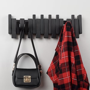 May include: Black wooden wall mounted coat rack with a red and black checked shirt and a black handbag hanging on it.